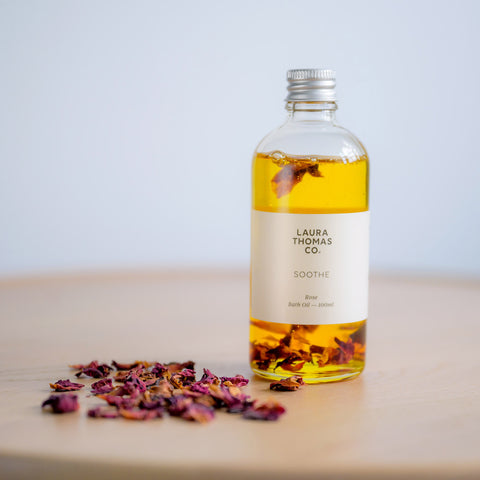 a glass bottle of rose bath oil with dried rose petals for a spa at home pamper