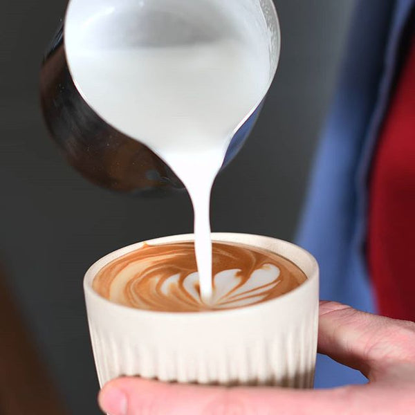 barista pouring flat white coffee into beige sustainable huskee coffee cup